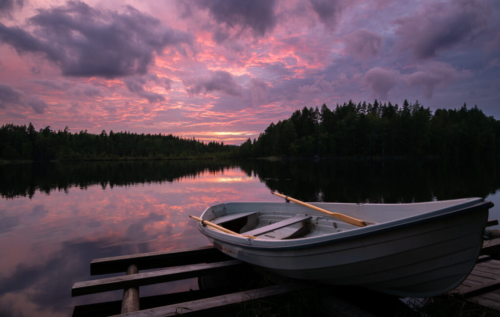 Ruhiger See in Finnland mit einem Bot am Land und farbigen Wolken.