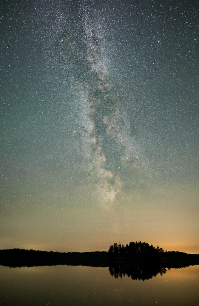 Milchstrasse über einem See mit einzelnen Spiegelungen.